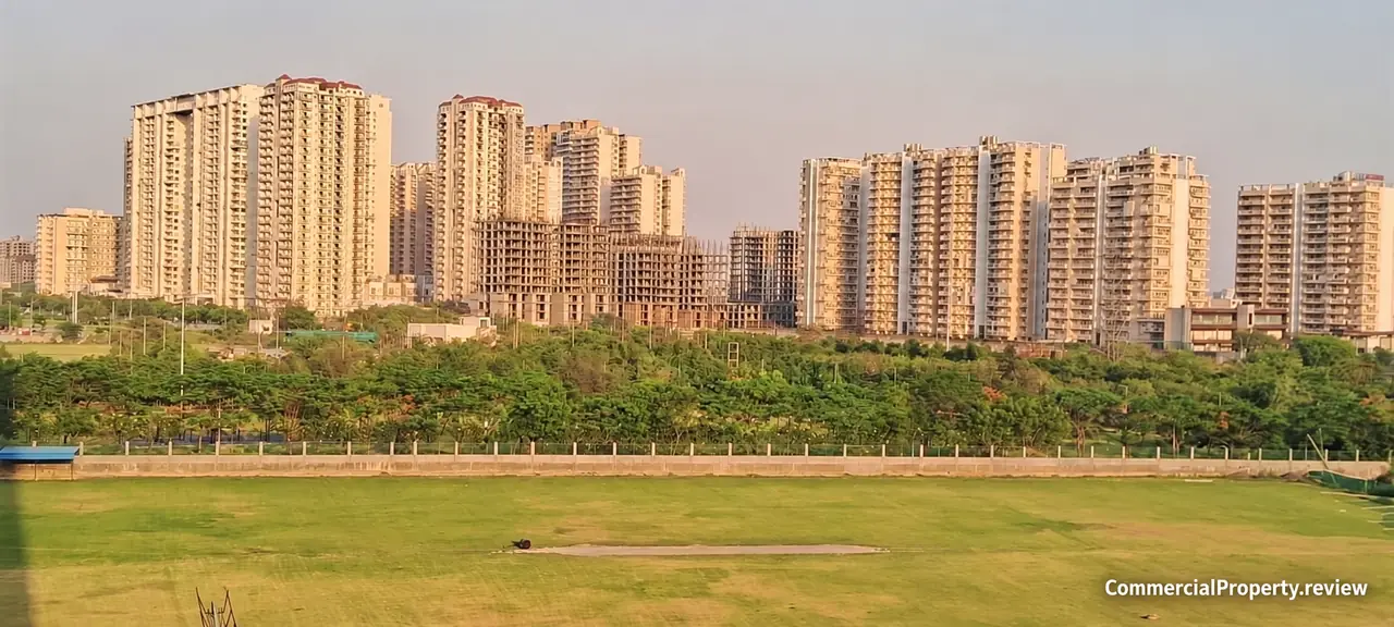 Residential towers overlooking trees and a sports ground in Central Noida